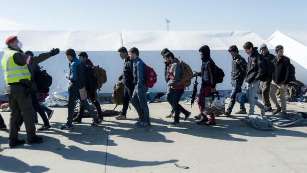 Eine Gruppe von Menschen geht an einem Kontrollpunkt vorbei, bewacht von einem Mann in Uniform.