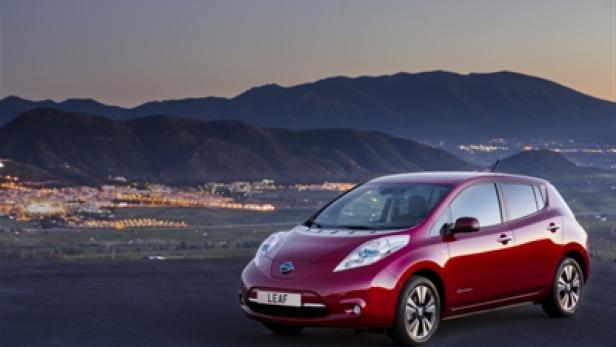 Ein roter Nissan Leaf vor einer Bergkulisse und einer beleuchteten Stadt.