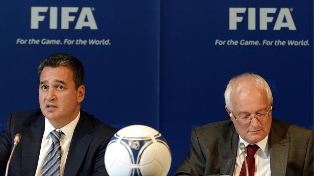 Zwei Männer sitzen an einem Tisch mit einem Fußball vor einem FIFA-Hintergrund.