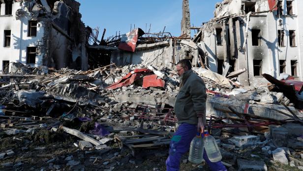 A man carries bottles of water as he walks past the building of a destroyed theatre in Mariupol