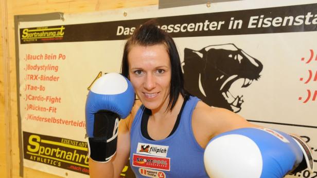 Eine Frau mit Boxhandschuhen vor einem Poster für ein Fitnesscenter in Eisenstadt.