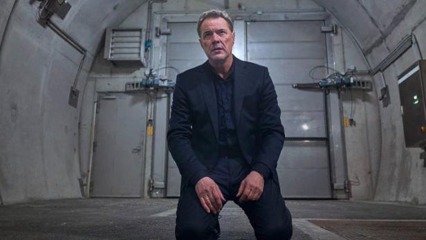 Ein Mann in Anzug kniet in einem unterirdischen Bunker.