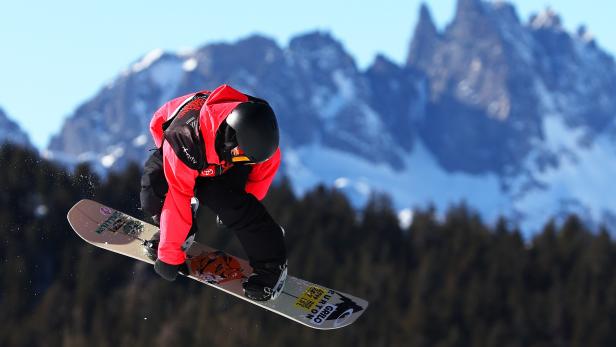 Ein Snowboarder springt vor einer Bergkulisse in der Luft.