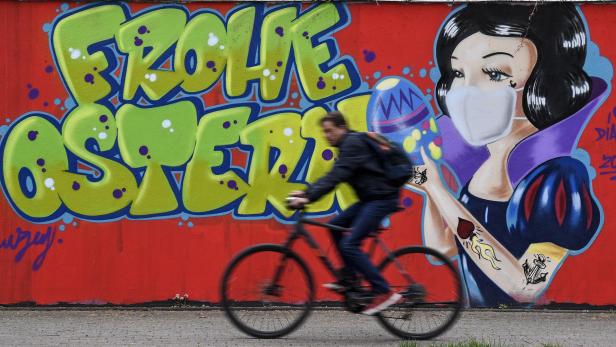 Ein Radfahrer fährt an einem Graffiti vorbei, das „Frohe Ostern“ und Schneewittchen mit Maske zeigt.