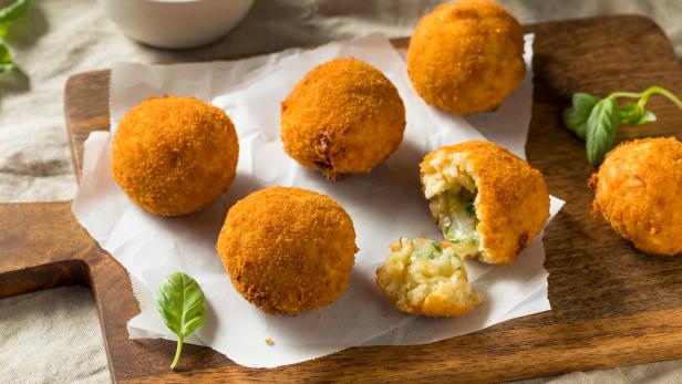 Mehrere goldbraune Arancini liegen auf einem Holzbrett mit Tomatensauce.