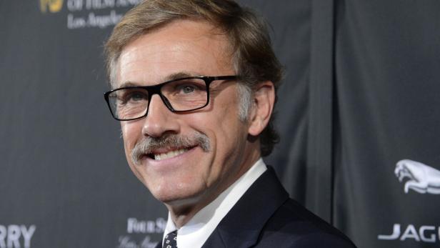 Porträt von Christoph Waltz mit Brille und Schnurrbart vor einem schwarzen Hintergrund.