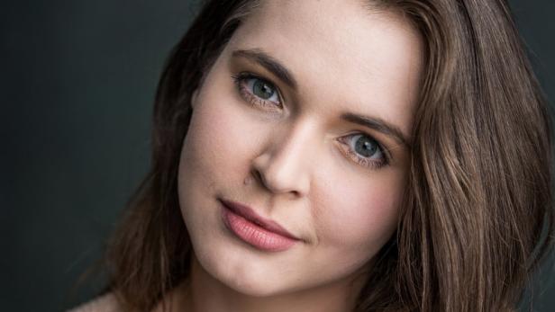 Porträt einer jungen Frau mit braunen Haaren und hellen Augen.