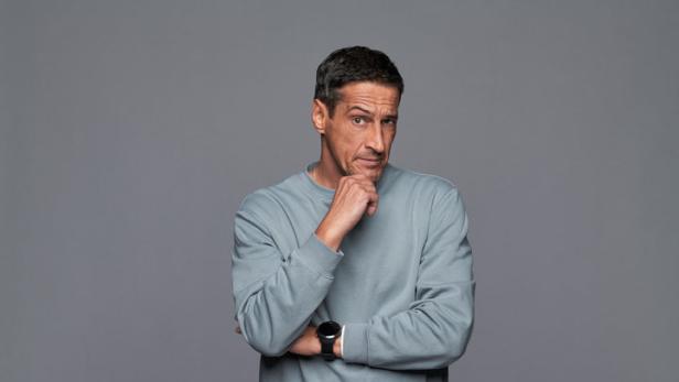 Ein Mann in Jeans, Pullover und Turnschuhen steht nachdenklich da.