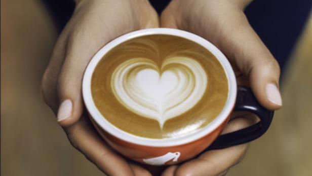 Eine Person hält eine rote Tasse mit einem Latte Art Herz.