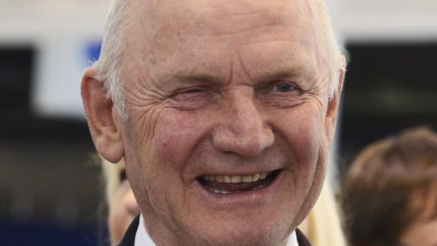 Ein älterer Mann mit weißem Haar zwinkert in die Kamera und lächelt.