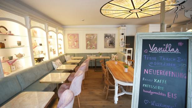 Innenansicht des Cafés „Vanillas“ mit Tischen, Stühlen und einer Tafel, die die Neueröffnung ankündigt.