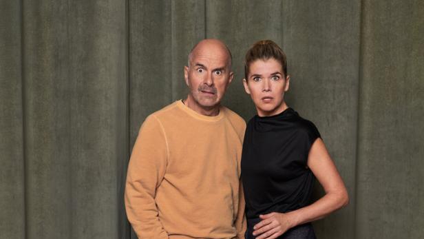 Ein Mann und eine Frau stehen vor einem grünen Vorhang und schauen überrascht in die Kamera.