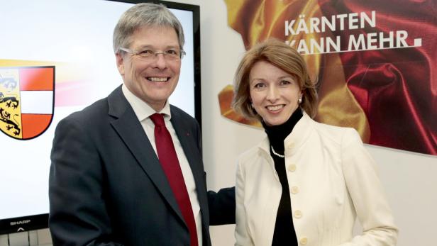 Ein Mann im Anzug und eine Frau in einer weißen Jacke lächeln in die Kamera.