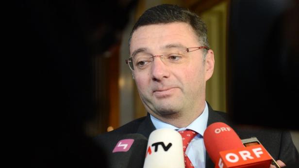 Ein Mann mit Brille wird von mehreren Mikrofonen interviewt.