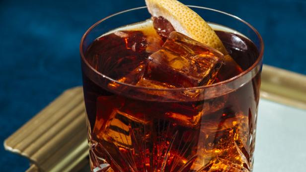 Ein Cocktail mit Eiswürfeln und einer Grapefruitzeste in einem Kristallglas.