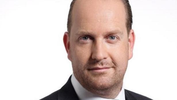 Porträt eines Mannes in Anzug und Krawatte vor einem weißen Hintergrund.