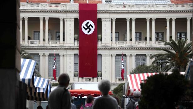 Ein Gebäude mit einer grossen Hakenkreuzfahne und kleineren Flaggen mit Hakenkreuzen davor.
