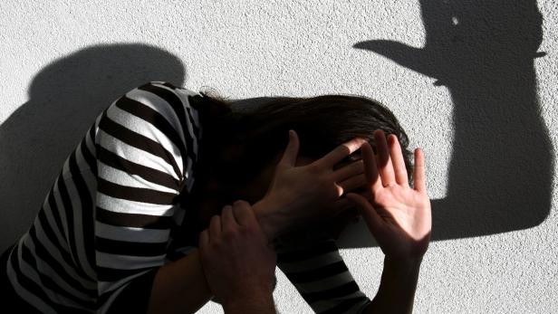 Eine Frau in einem gestreiften Oberteil schützt ihr Gesicht mit den Händen vor einem Schatten an der Wand.