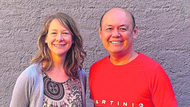 Eine Frau mit langen Haaren und ein Mann mit einem roten T-Shirt lächeln in die Kamera.