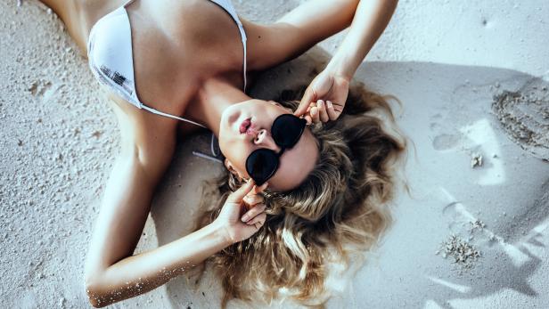 Eine Frau mit Sonnenbrille liegt am Strand im Sand.