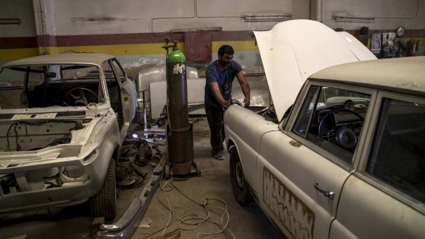 Ein Mechaniker arbeitet in einer Werkstatt an einem Oldtimer mit geöffneter Motorhaube.