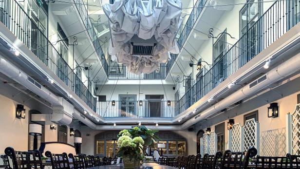 Ein Innenhof mit Tischen und Stühlen unter einem großen, dekorativen Deckenelement.
