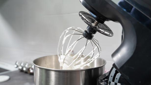 open black Electric stand mixer on a table in the kitchen with white cream