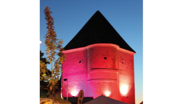 Ein roter Turm mit schwarzem Dach wird von unten angestrahlt.