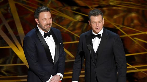 Ben Affleck und Matt Damon in Anzügen auf einer Bühne.