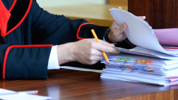 Ein Richter in Robe blättert mit einem Stift in einem Stapel Akten.