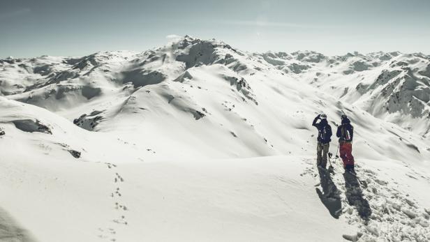 Zwei Skifahrer blicken auf eine weite, schneebedeckte Berglandschaft.