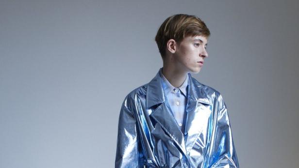 Ein Mann trägt einen glänzenden, silberblauen Trenchcoat mit passenden Stiefeln.