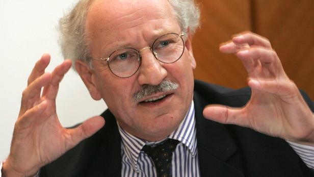 Ein Mann mit Brille und Schnurrbart gestikuliert mit beiden Händen.