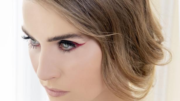 Eine Frau mit rotem Eyeliner und einer Halskette mit Blumenmuster blickt nach links.