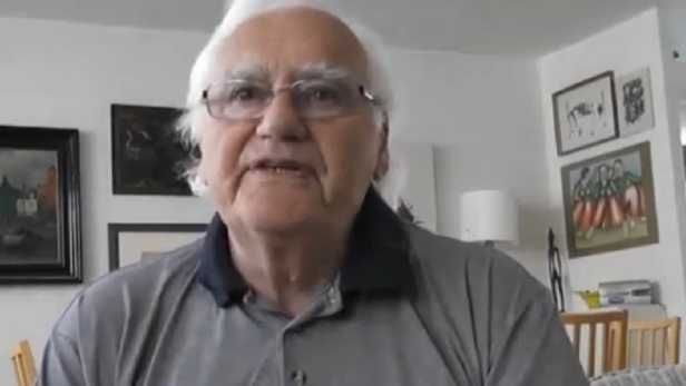 Ein älterer Mann mit Brille und weißem Haar spricht vor der Kamera.