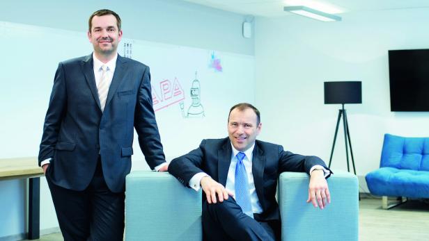 Zwei Männer in Anzügen posieren in einem modernen Büro.