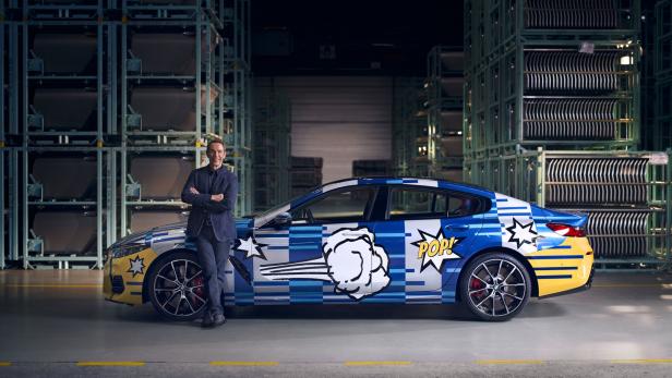 Ein Mann posiert vor einem BMW mit Pop-Art-Design in einer Lagerhalle.