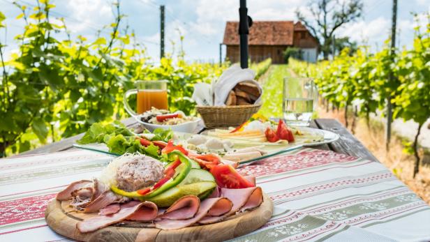 Eine Brettljause, eine kalte Platte mit Speisen, auf einem Holztisch im Weinberg.