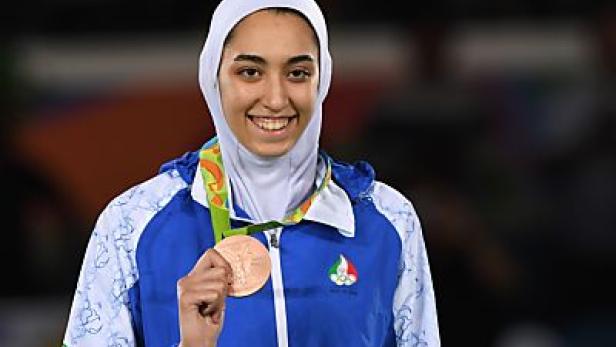 Eine lächelnde Frau mit Hijab präsentiert stolz ihre Bronzemedaille.