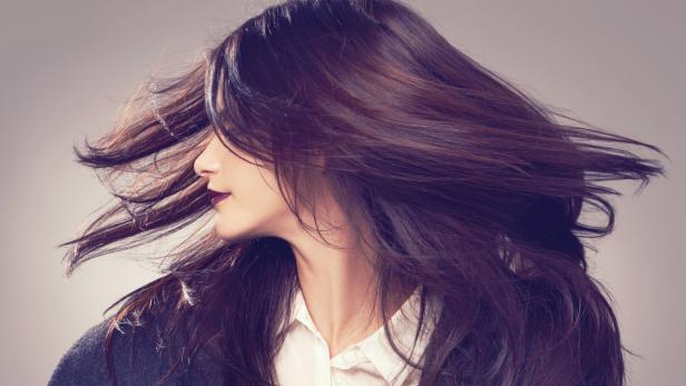 Eine Frau mit dunklen Haaren und dunklem Lippenstift, deren Haare im Wind wehen.