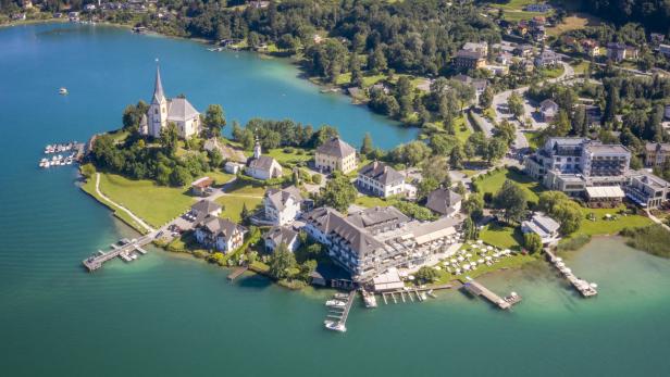 Luftaufnahme von Maria Wörth am Wörthersee mit Bergen im Hintergrund.