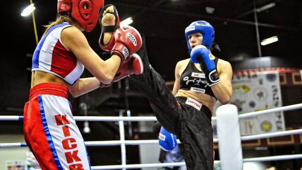 Zwei Kickboxerinnen kämpfen im Ring, eine tritt mit dem Bein nach vorne.