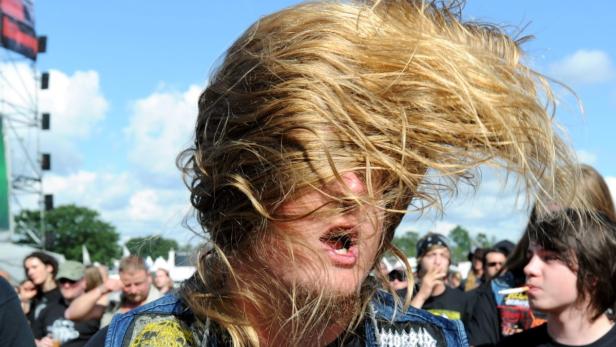Ein Mann mit langen blonden Haaren headbangt auf einem Heavy-Metal-Konzert.