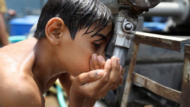Ein Bub trinkt aus einer Wasserleitung in Neu Delhi