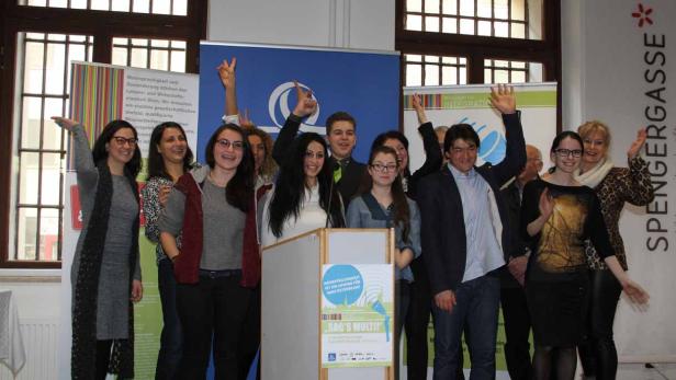 Eine Gruppe von Menschen steht hinter einem Rednerpult und winkt in die Kamera.