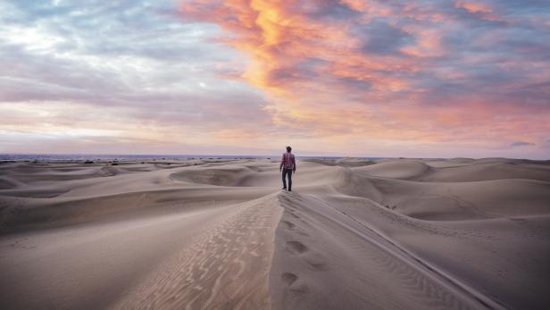Ein Mann steht auf einer Sanddüne und blickt auf die Landschaft bei Sonnenuntergang.