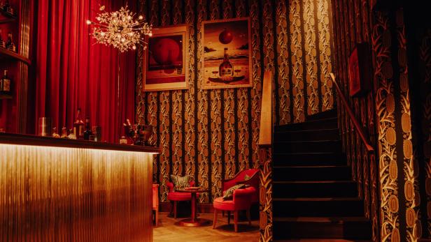Eine Bar mit roten Samtvorhängen, gemusterter Tapete und einer Treppe.