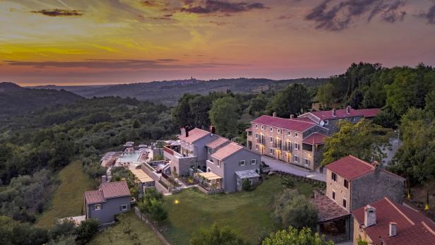 Luftaufnahme eines Resorts mit mehreren Gebäuden, einem Pool und üppigem Grün bei Sonnenuntergang.