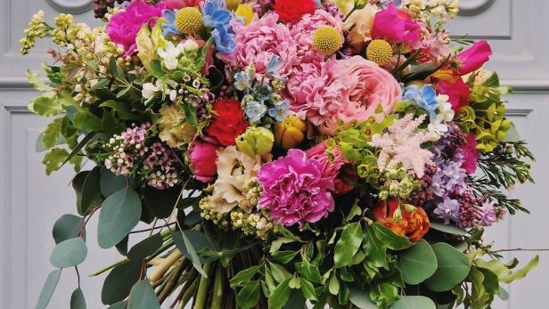 Ein bunter Blumenstrauß wird vor einer grauen Tür gehalten.