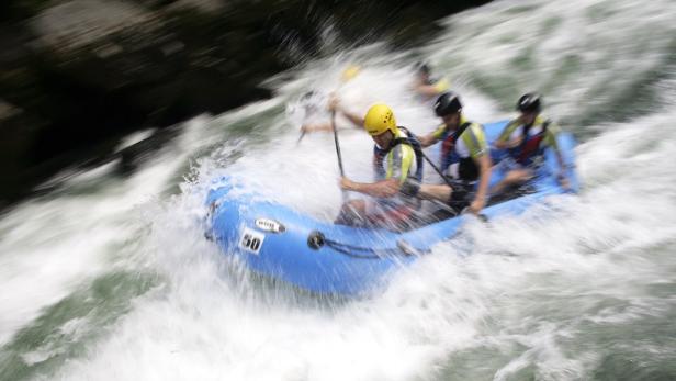 Eine Gruppe von Personen raftet auf einem blauen Schlauchboot durch reißendes Wasser.